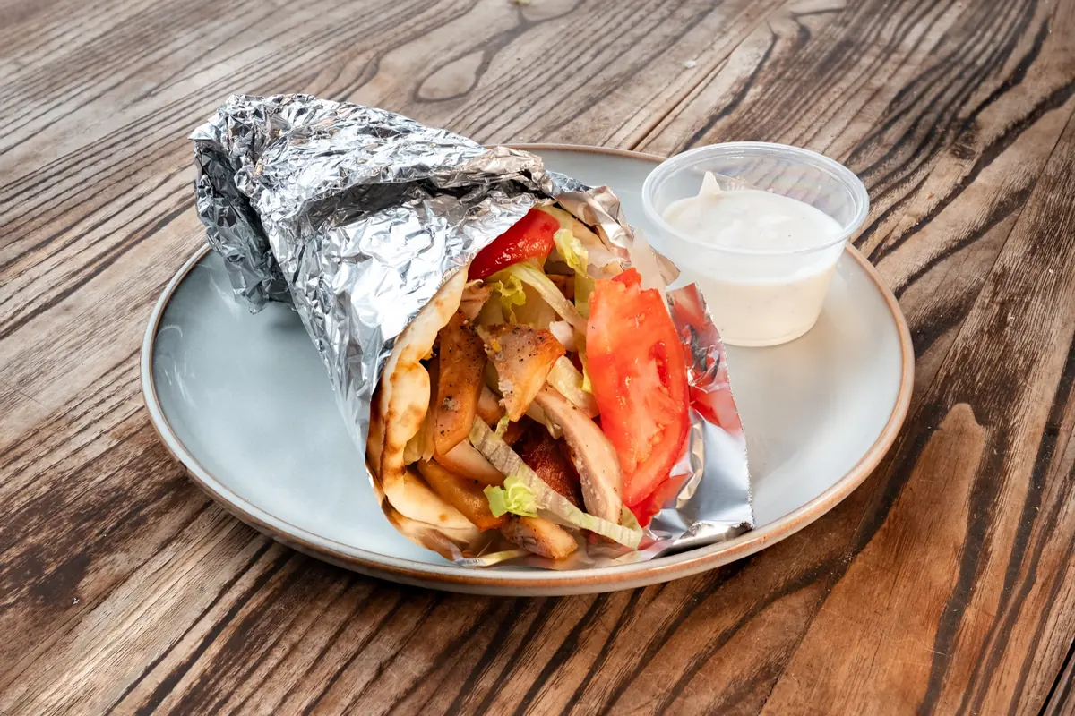 Chicken gyro in pita with tomato and a cup of white sauce