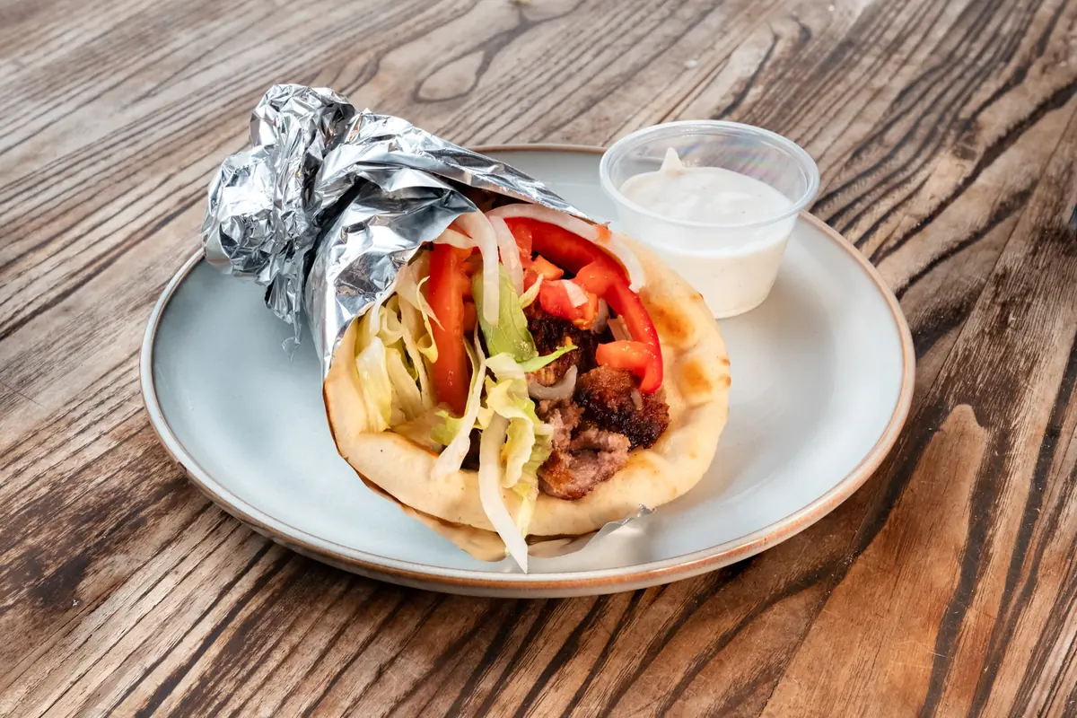 Lamb gyro wrapped in pita and foil with tomato, onion and white sauce