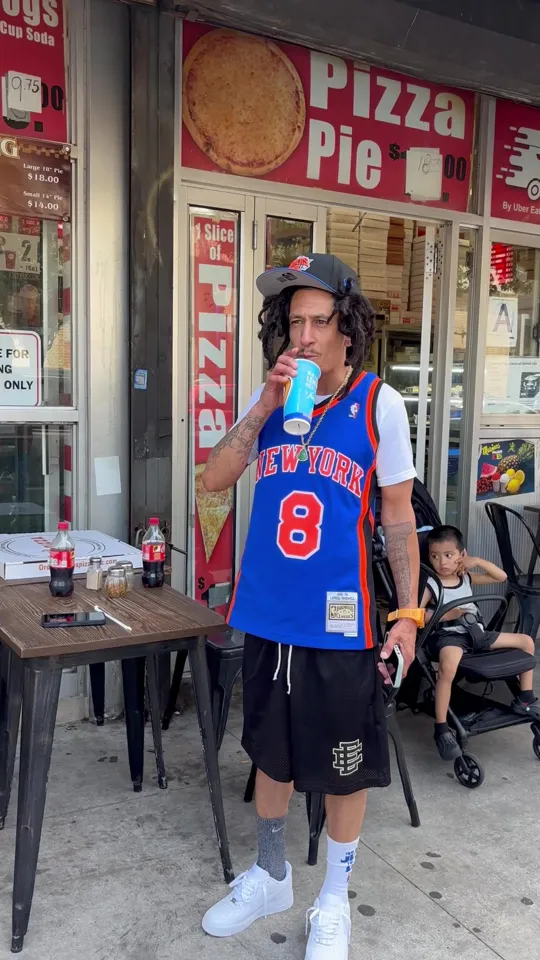 Stormi on the sidewalk with a drink and a slice